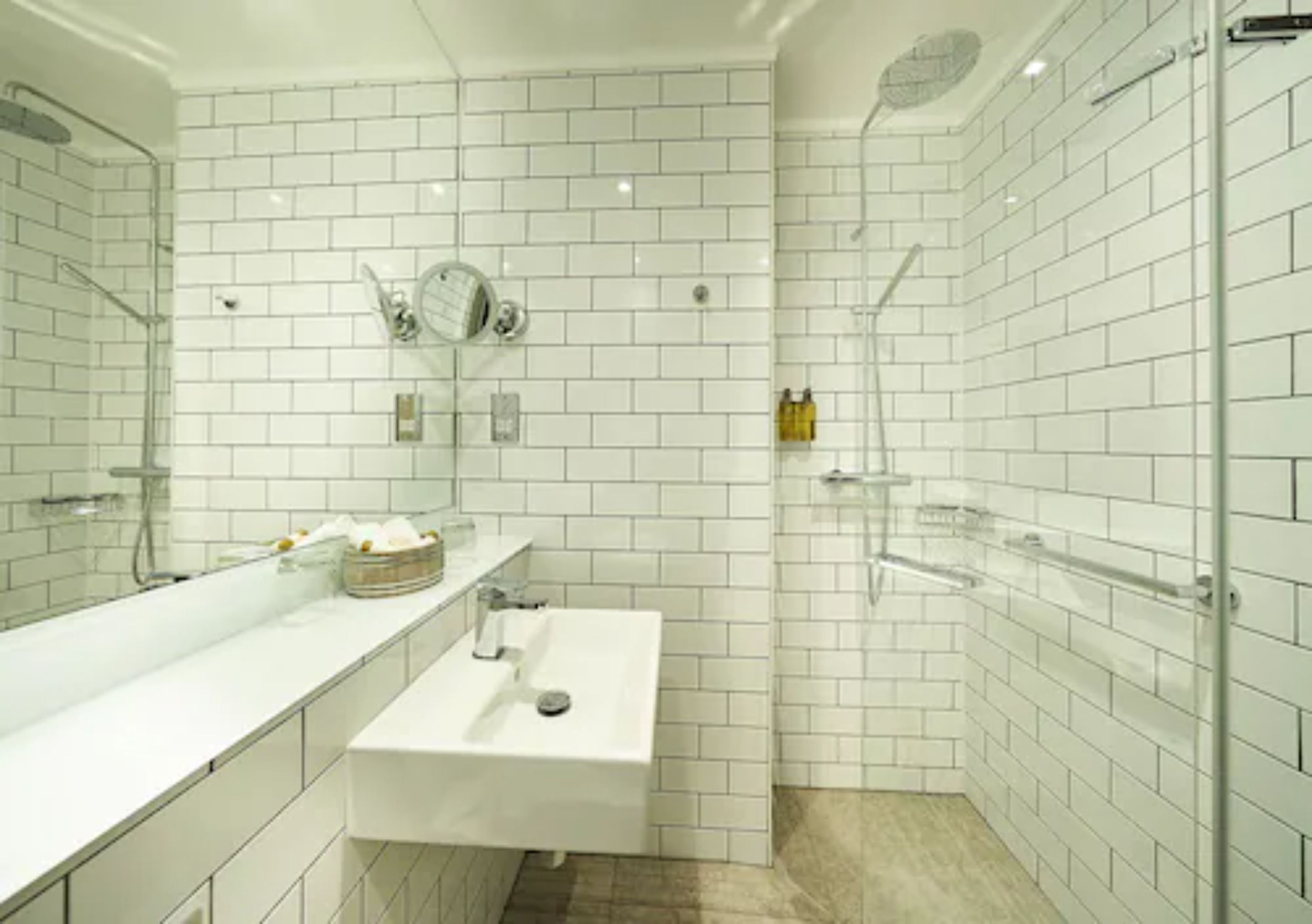 Un baño moderno con azulejos blancos tipo metro, un lavamanos blanco, un espejo y una cabina de ducha de vidrio.