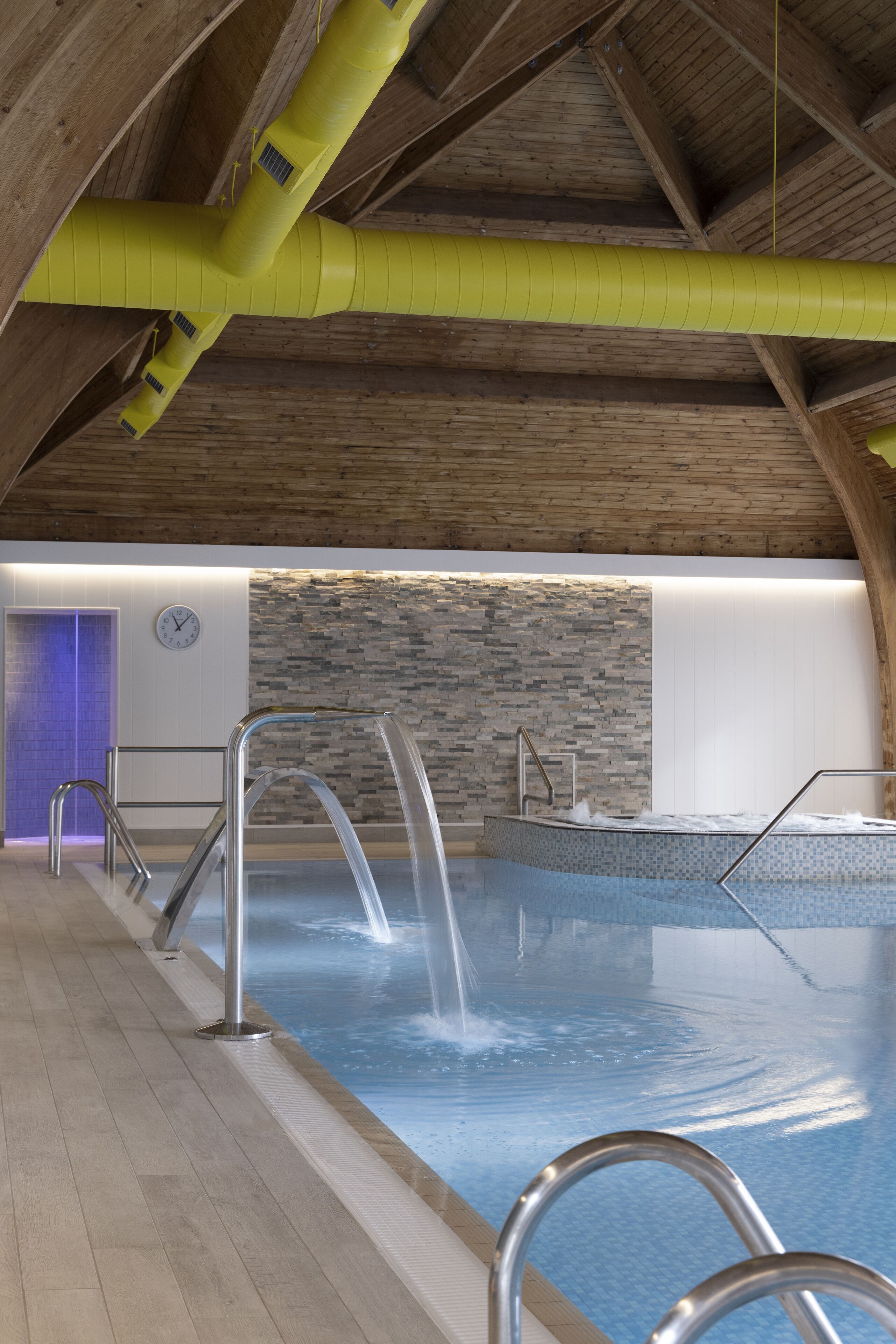 Una piscina interior con pared de piedra y vigas de madera.
