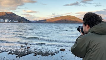 Una persona fotografiando un lago con montañas al fondo.