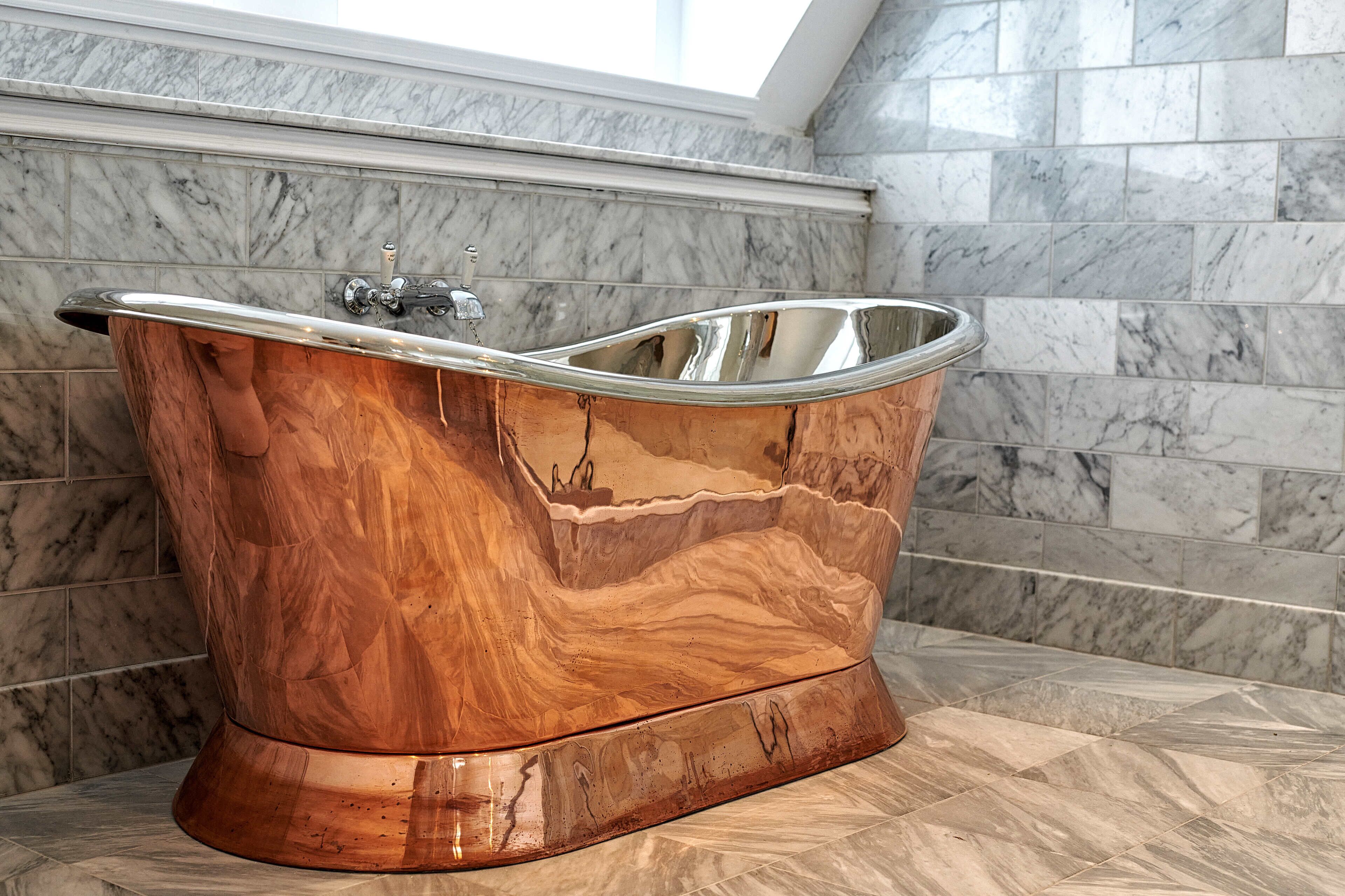 A freestanding bathtub with a wooden finish in a bathroom with marble walls and floor.