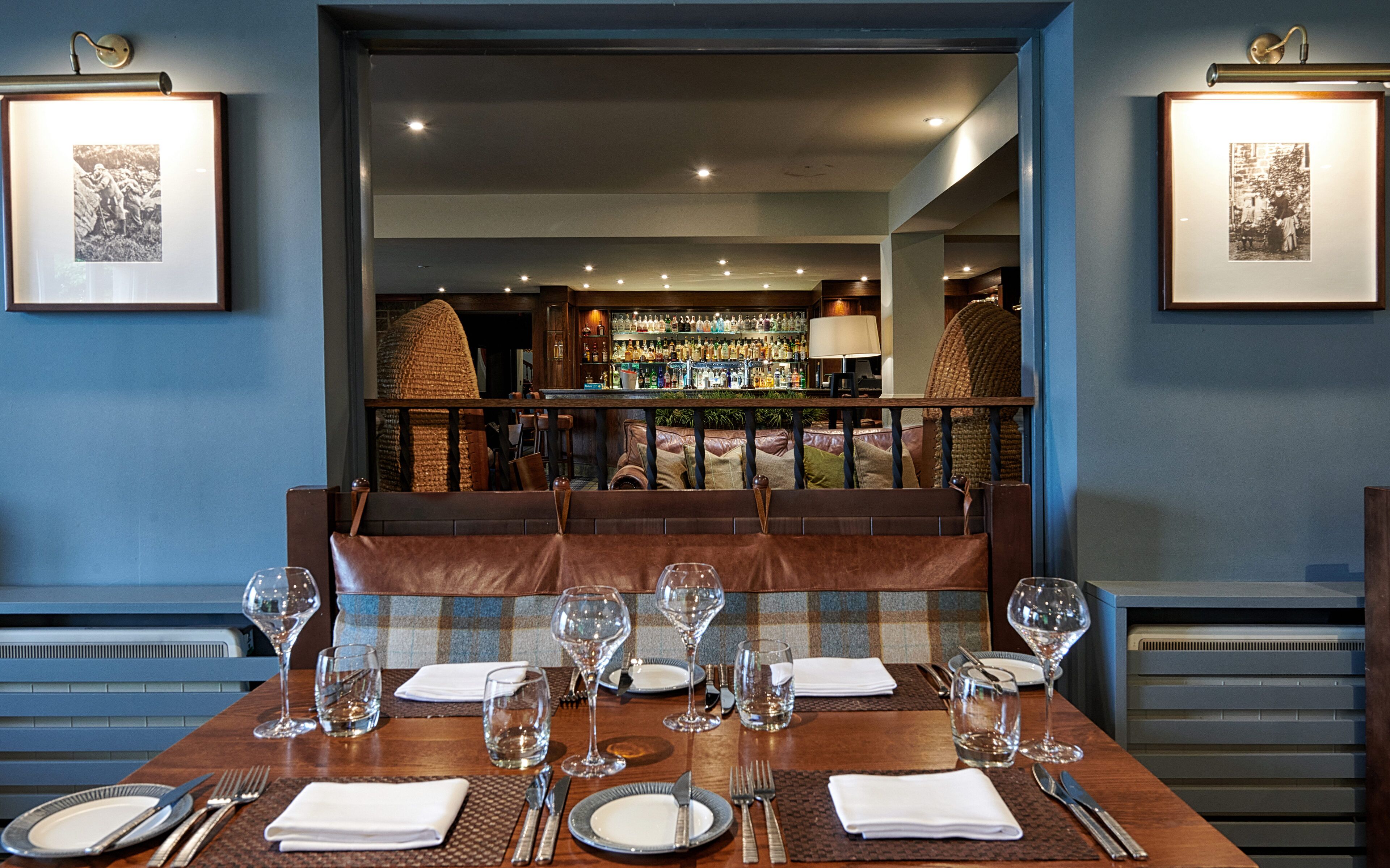 Un coin repas avec une table dressée pour six personnes, un bar en arrière-plan et des tableaux encadrés accrochés aux murs.