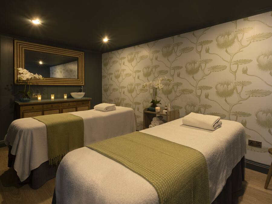 A room with two beds, a large mirror, a vanity with a bowl sink, and a floral wallpaper.