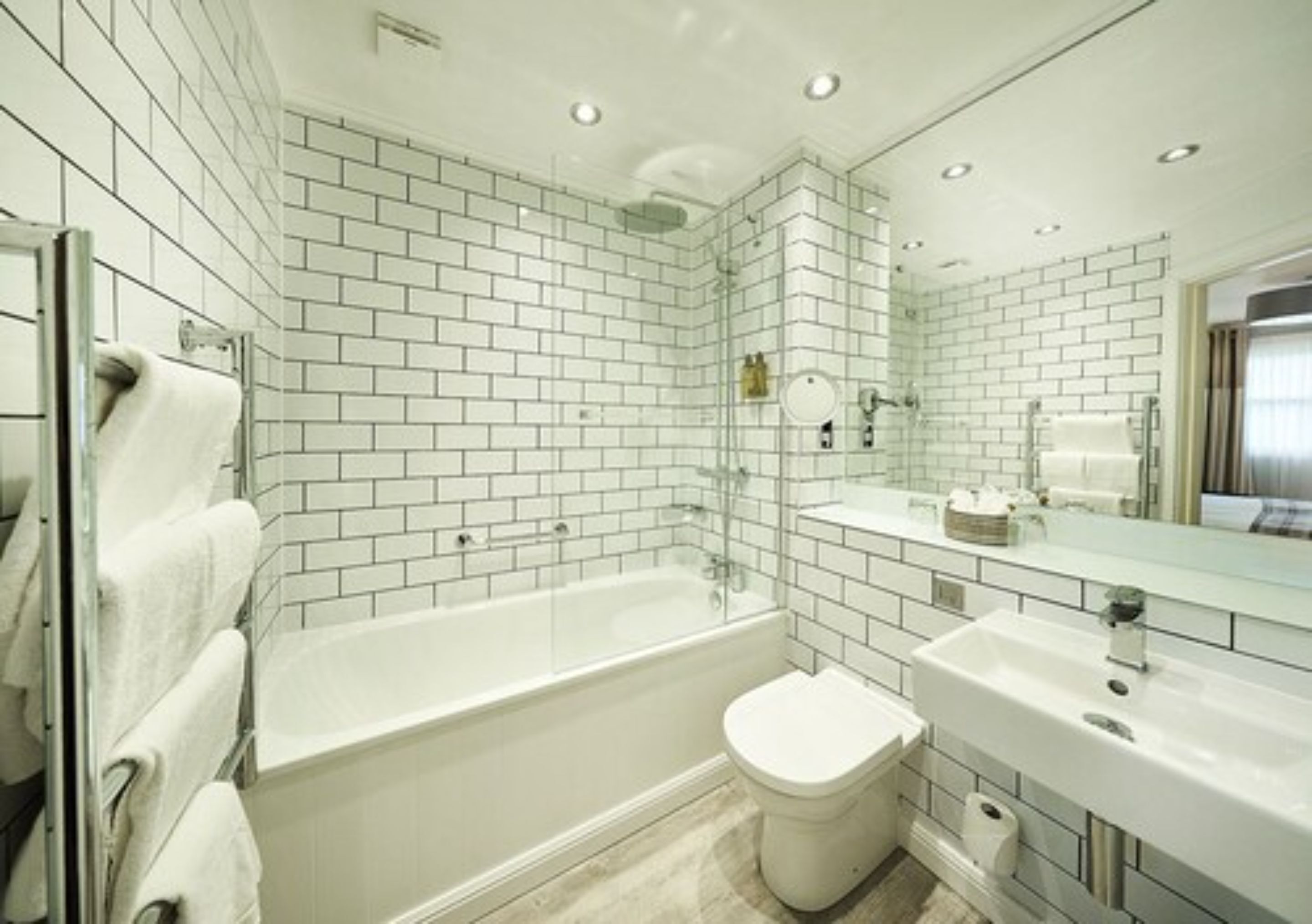 A modern bathroom with white subway tiles, a bathtub, a toilet, and a sink.