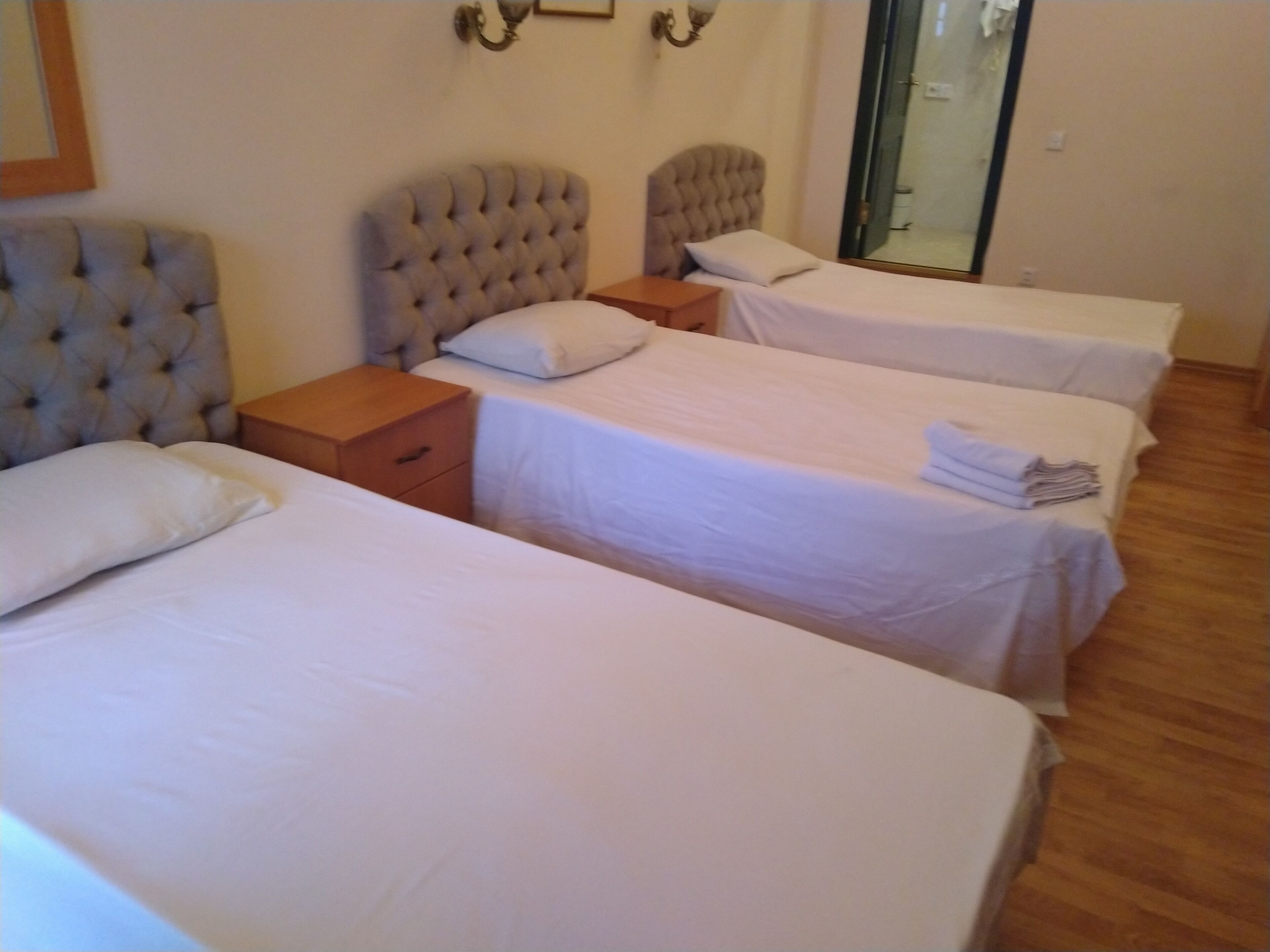 Une chambre d’hôtel avec trois lits simples, chacun doté d’une table de chevet en bois et d’un oreiller blanc.