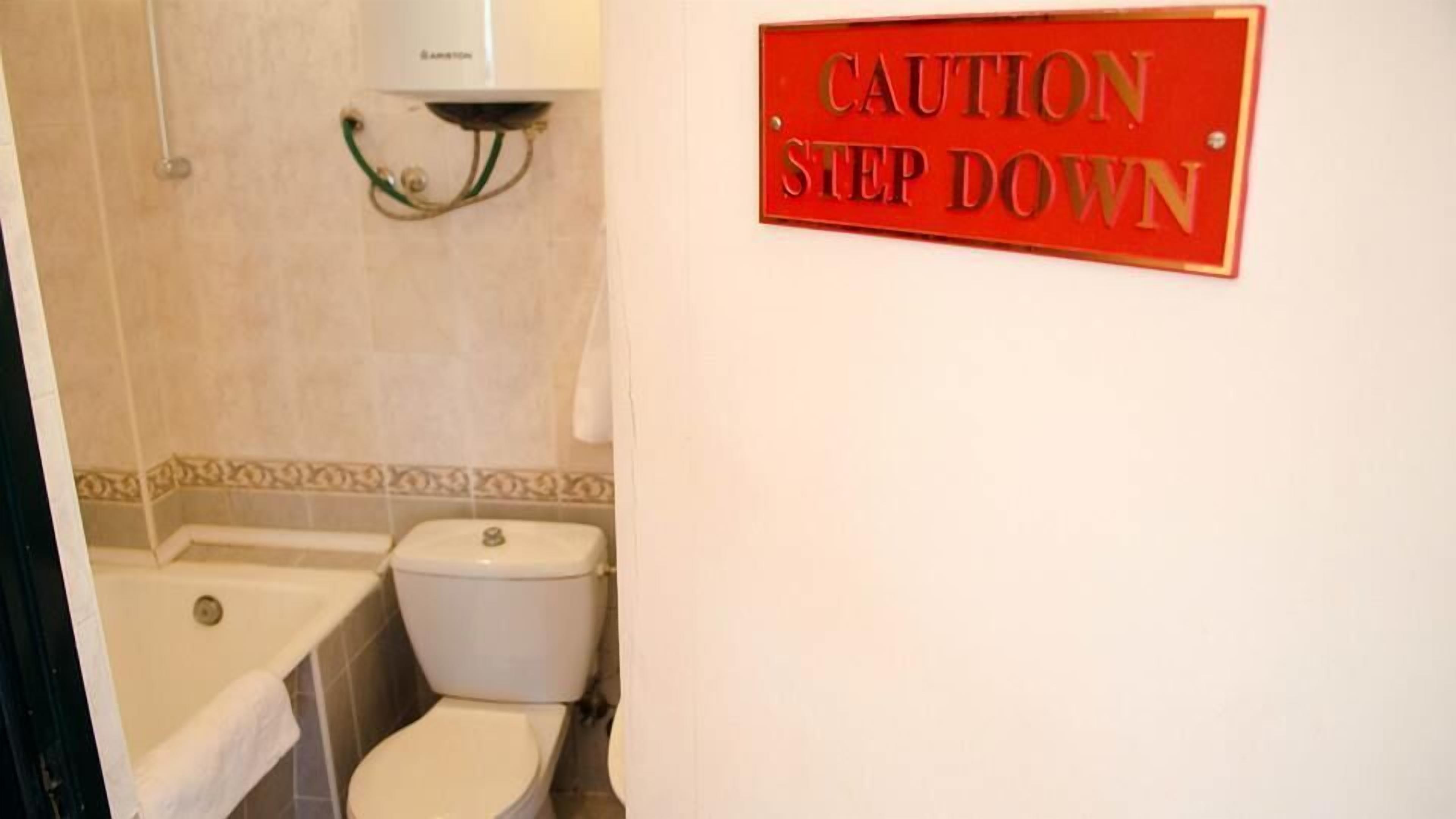 Un baño con inodoro, lavabo y un letrero de precaución.