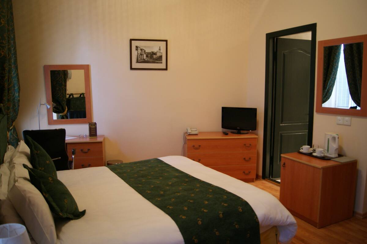 Een hotelkamer met een bed, een dressoir, een televisie, een bureau met een stoel, en een deur.