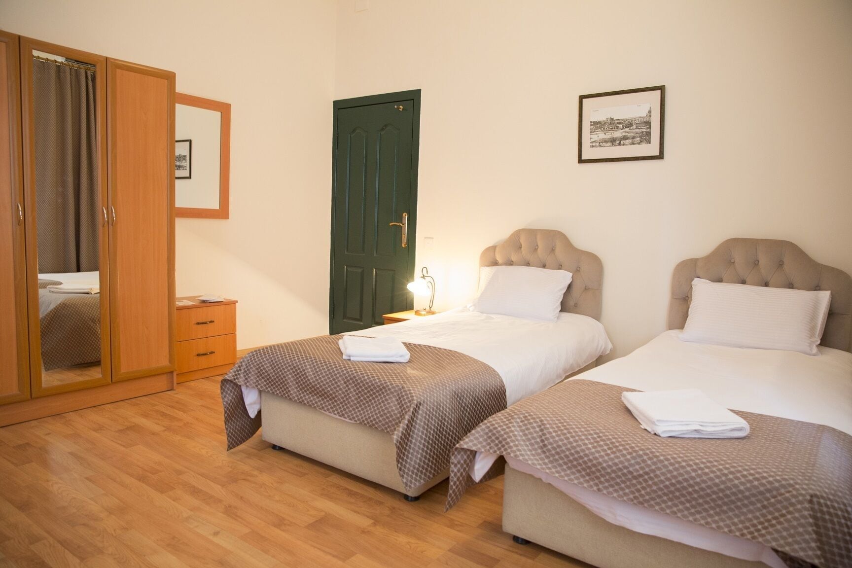 A hotel room with two beds, a wardrobe, a door, and a framed picture on the wall.