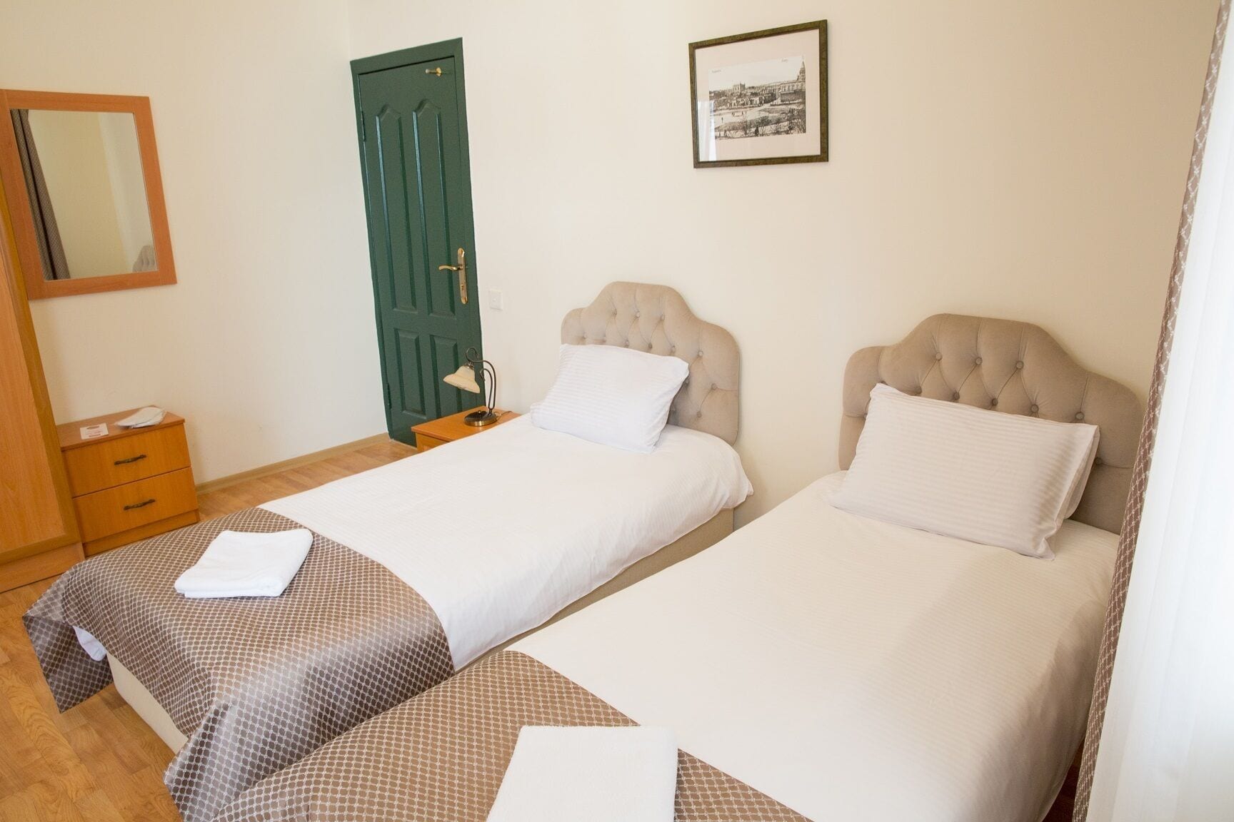 A double room with two beds, a wooden dresser, a green door, and a framed picture on the wall.