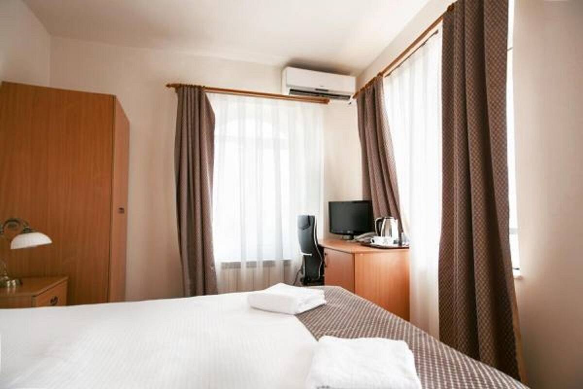 Een hotelkamer met een bed, een bureau met een computer, een lamp en gordijnen.