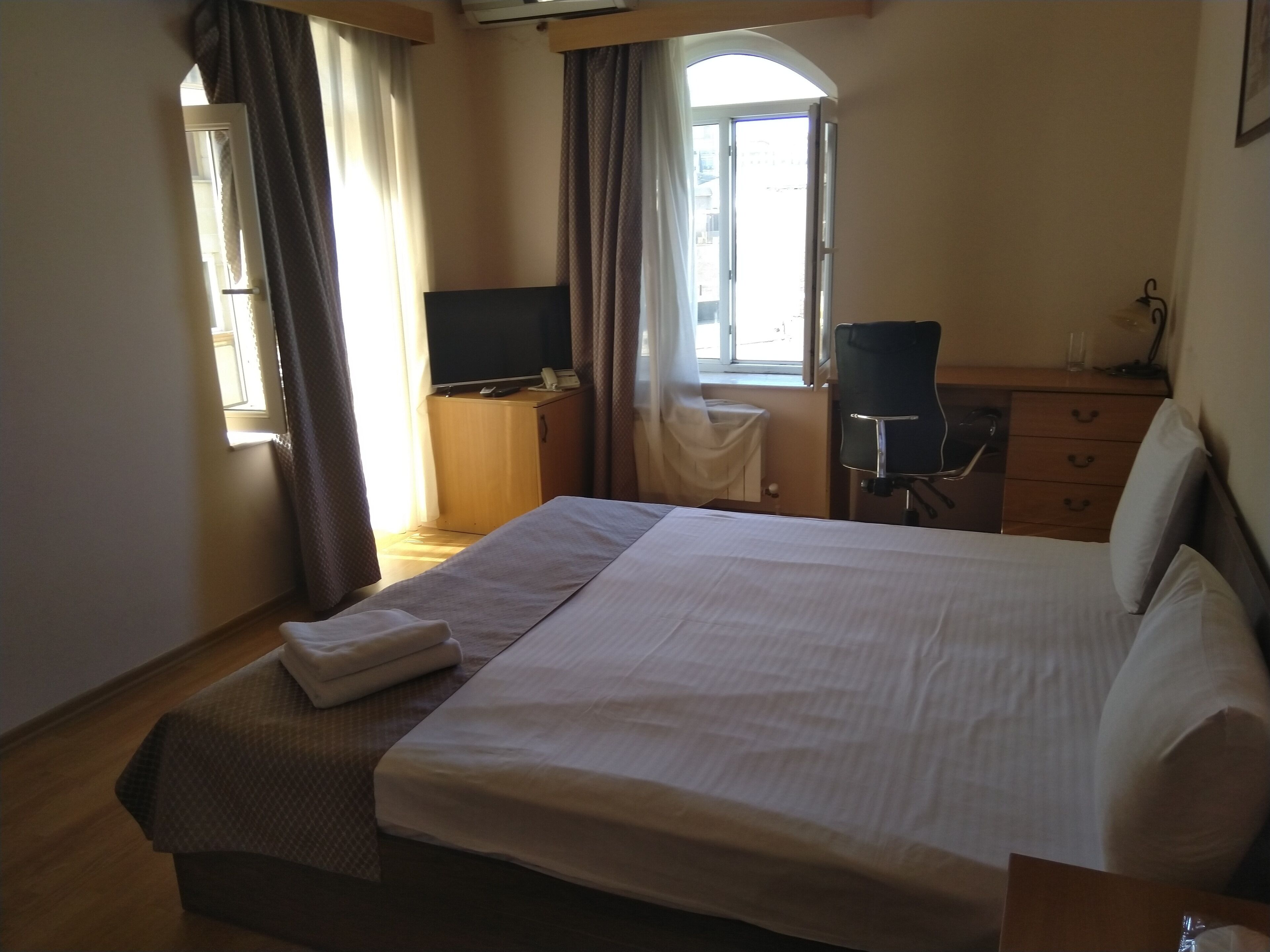 A hotel room with a large bed, a desk with a chair, a television, and a window with curtains.