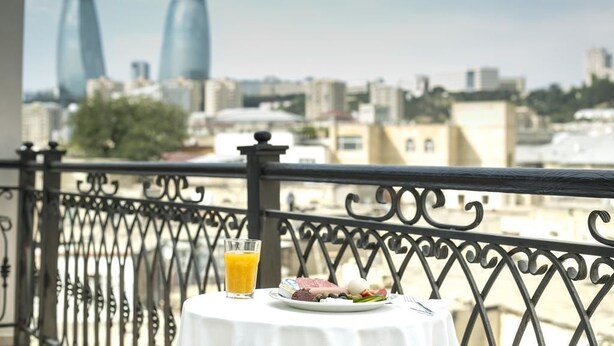A balcony with a table set for breakfast, featuring a glass of orange juice and a plate of food. - Old City Inn Hotel (Baku)