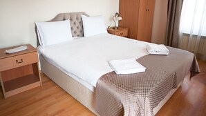 Een keurig opgemaakt bed met een wit-bruin dekbedovertrek, een bedlampje en een houten nachtkastje met een lade.
