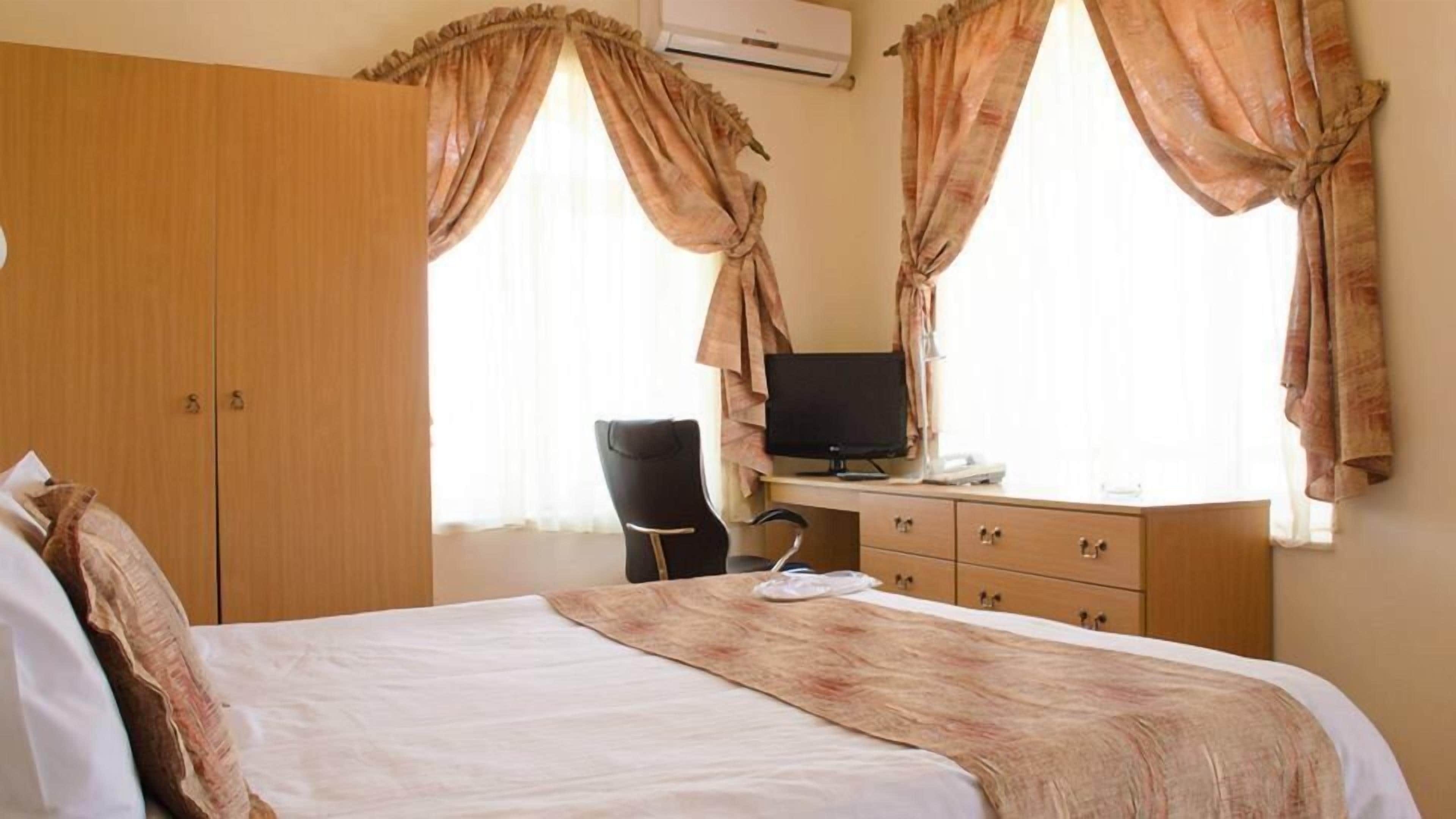 A hotel room with a bed, a desk with a computer, and a chair.