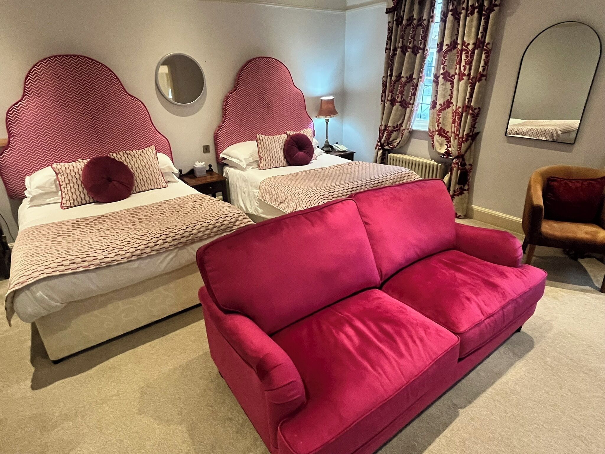 A hotel room with two beds, a red sofa, and a mirror on the wall.