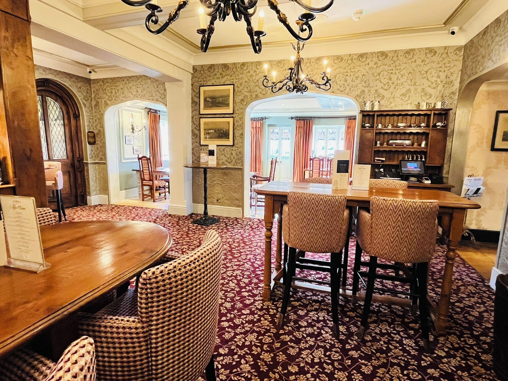 A dining area with a wooden table and wicker chairs, a chandelier, and a patterned carpet.