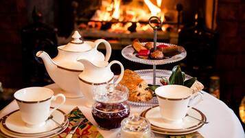 A tea service set with a teapot, cups, and saucers, along with pastries and jam on a table.