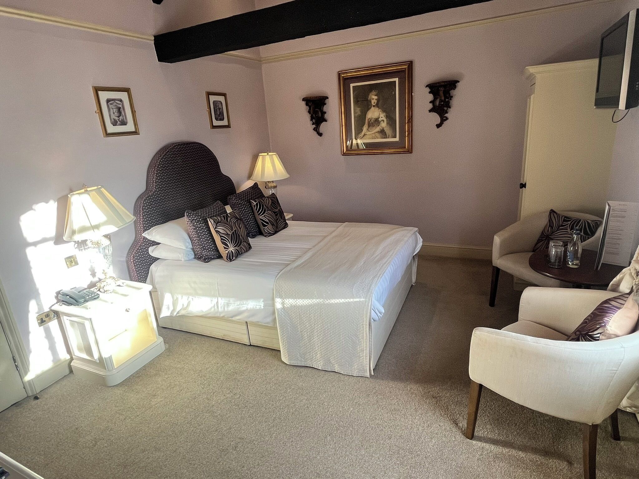 A neatly arranged bedroom with a bed, bedside lamps, a chair, and wall-mounted artwork.