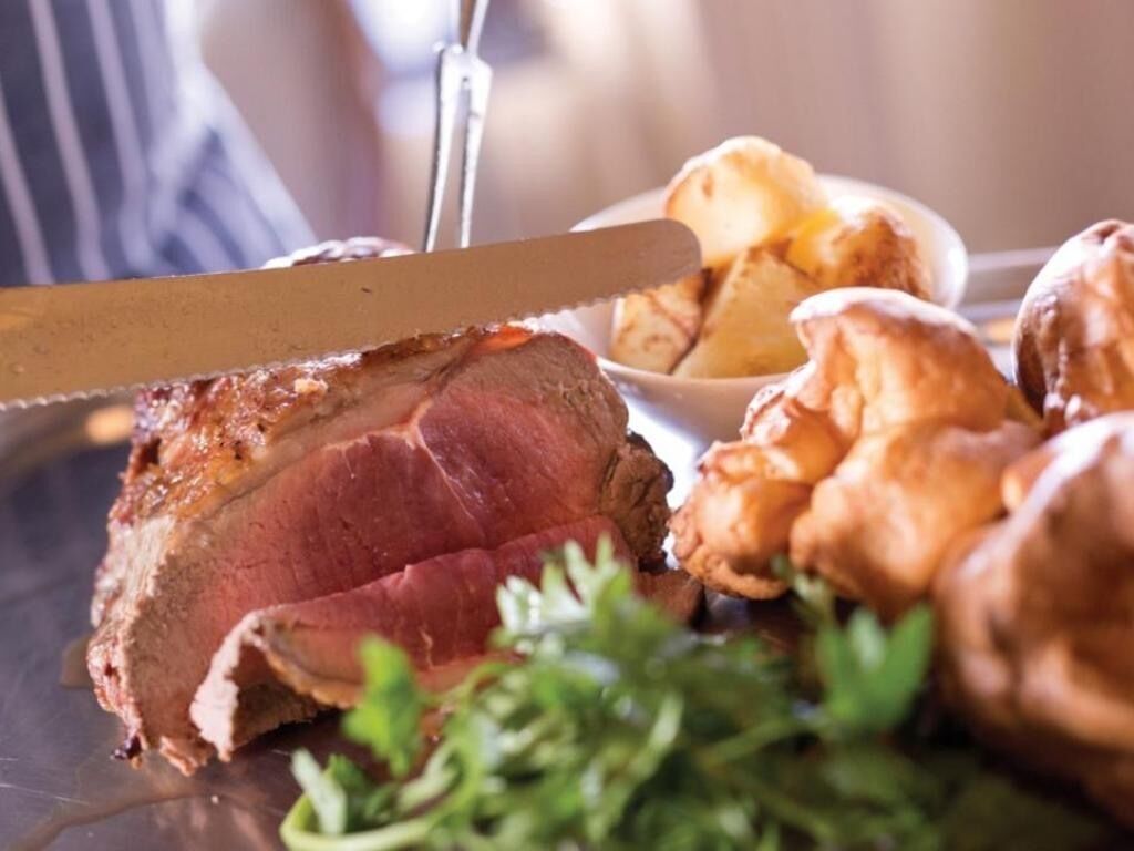 A steak with a knife, surrounded by roasted potatoes and greens.