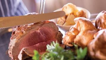 A steak with a knife, surrounded by roasted potatoes and greens.