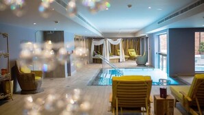 Un área de piscina interior moderna con sillones de descanso, barandilla de vidrio y vistas al exterior.