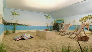 Habitación con temática de playa, que cuenta con una terraza de madera, dos sillas reclinables a rayas, una mesita y un letrero que dice 'Life's at Ease with an Ocean Breeze'.