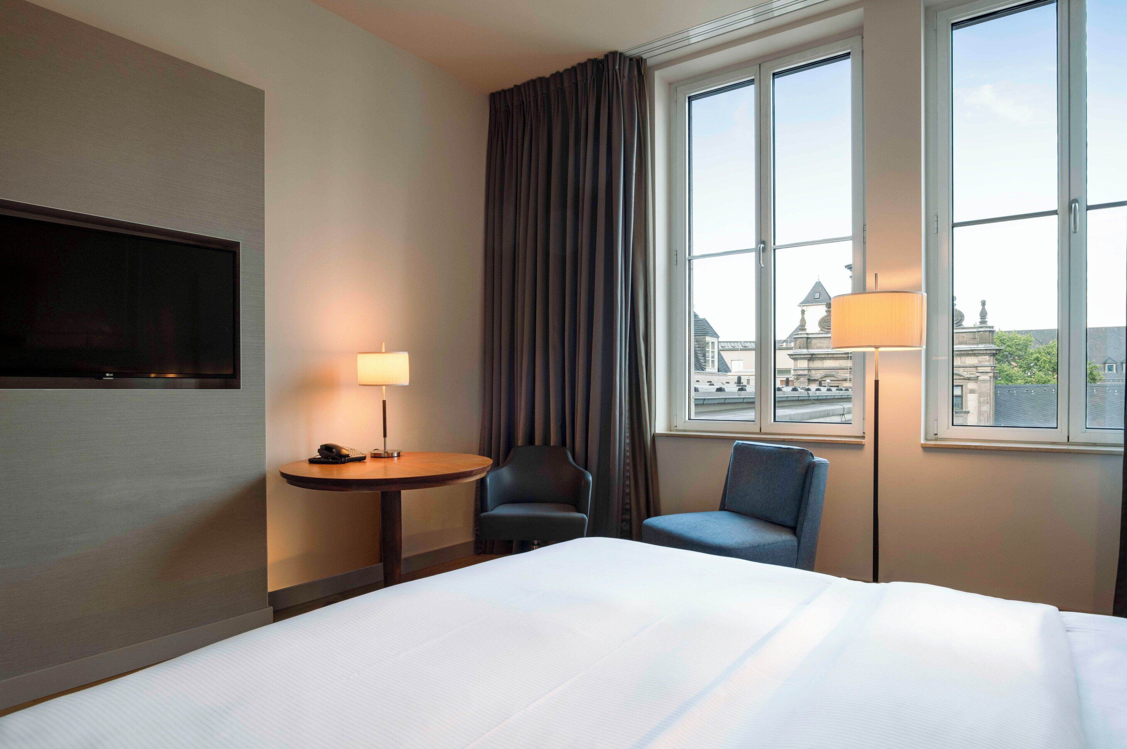 Een hotelkamer met een bed, een bureau met lamp, twee stoelen en een televisie.