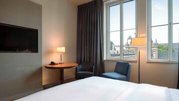A hotel room with a bed, a desk with a lamp, two chairs, and a TV.