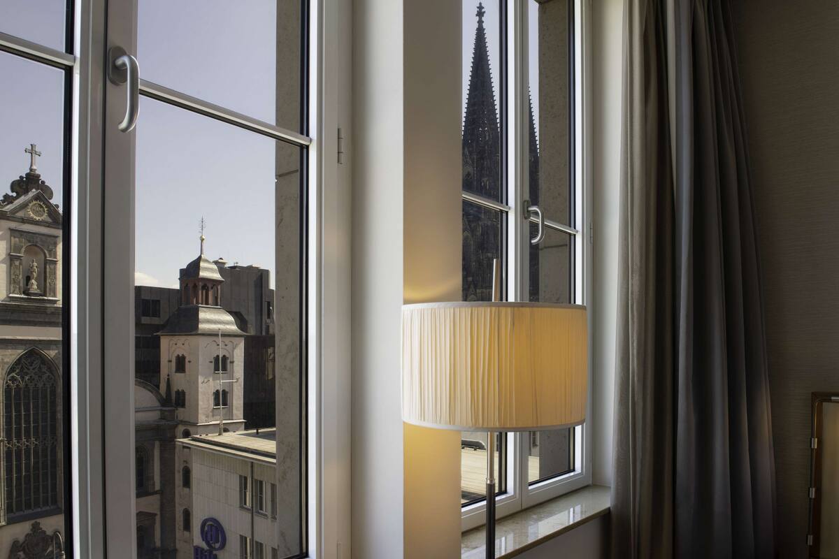 Una habitación con un ventanal grande, una lámpara y vistas a un edificio con aguja.