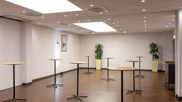 Une salle de conférence moderne dotée d’un plancher en bois, de luminaires encastrés et de plusieurs tables aux pieds en métal noir.