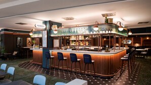 Zona de bar con mostrador de madera, taburetes y una variedad de botellas.