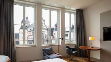 Habitación de hotel con cama, escritorio, silla y ventanas amplias con vista a la ciudad.