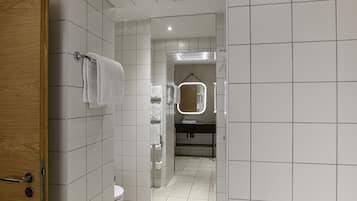 Un baño moderno con azulejos blancos, una puerta de madera, un espejo con iluminación y una zona de ducha.