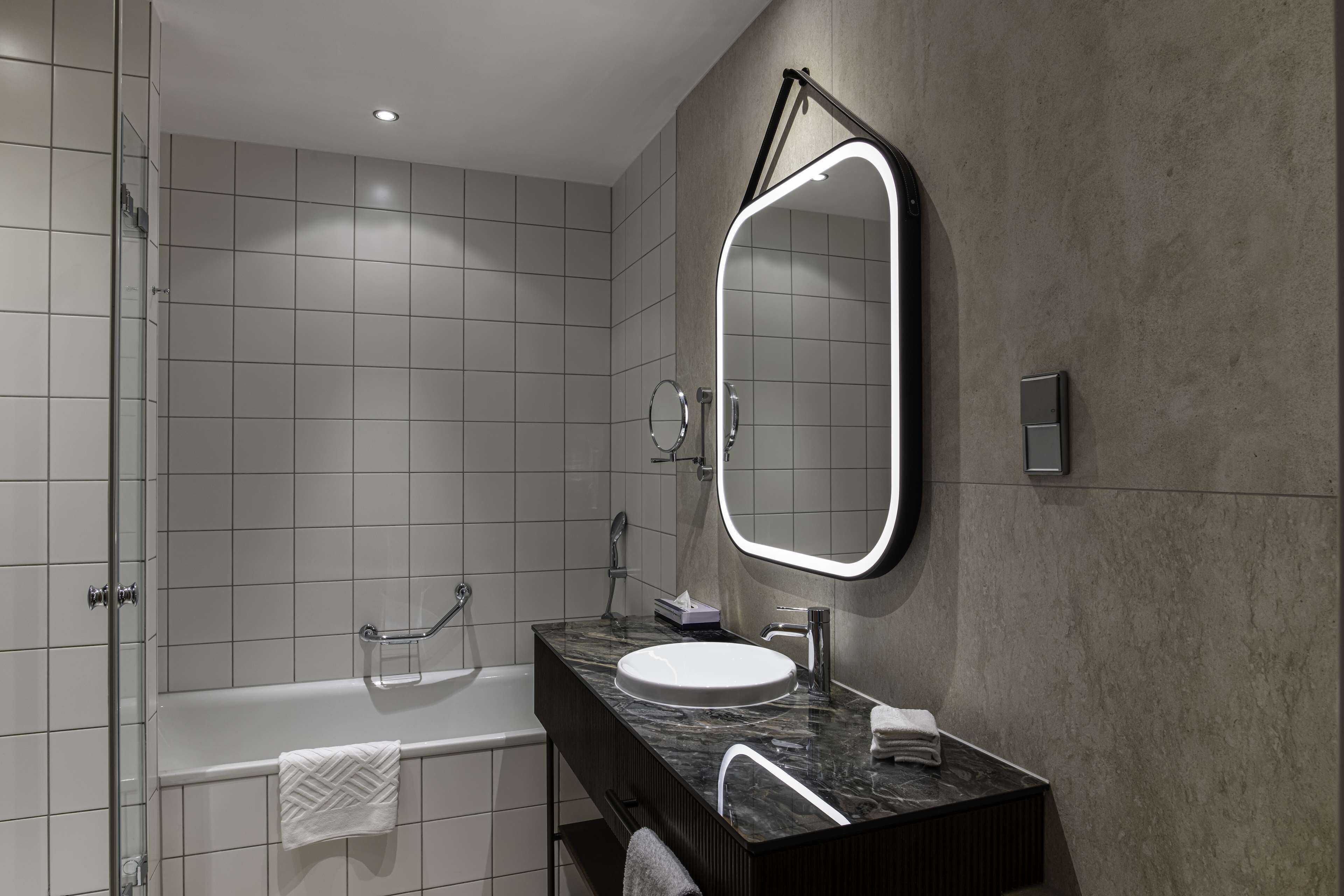 A modern bathroom with a large mirror, a bathtub, and a vanity with a sink.