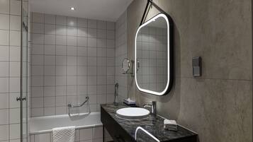 A modern bathroom with a large mirror, a bathtub, and a vanity with a sink.
