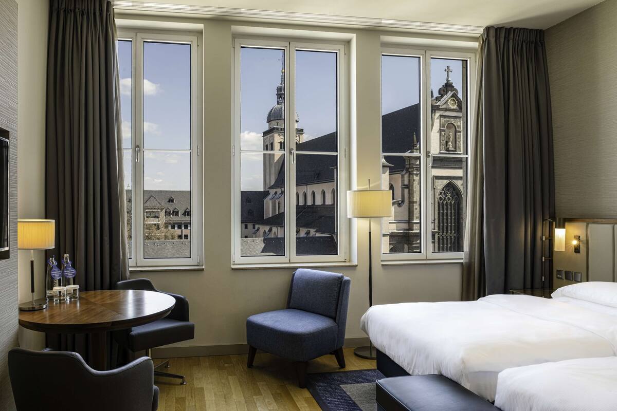 Una habitación de hotel con un ventanal grande, una cama, un escritorio y una silla.