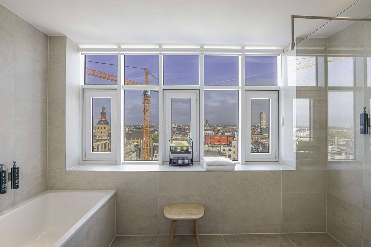 Un baño moderno con un ventanal grande, una bañera y un taburete de madera.