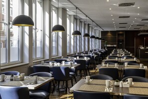 Un espace de restauration moderne, doté de longues tables et de chaises, de grandes fenêtres et de luminaires suspendus.