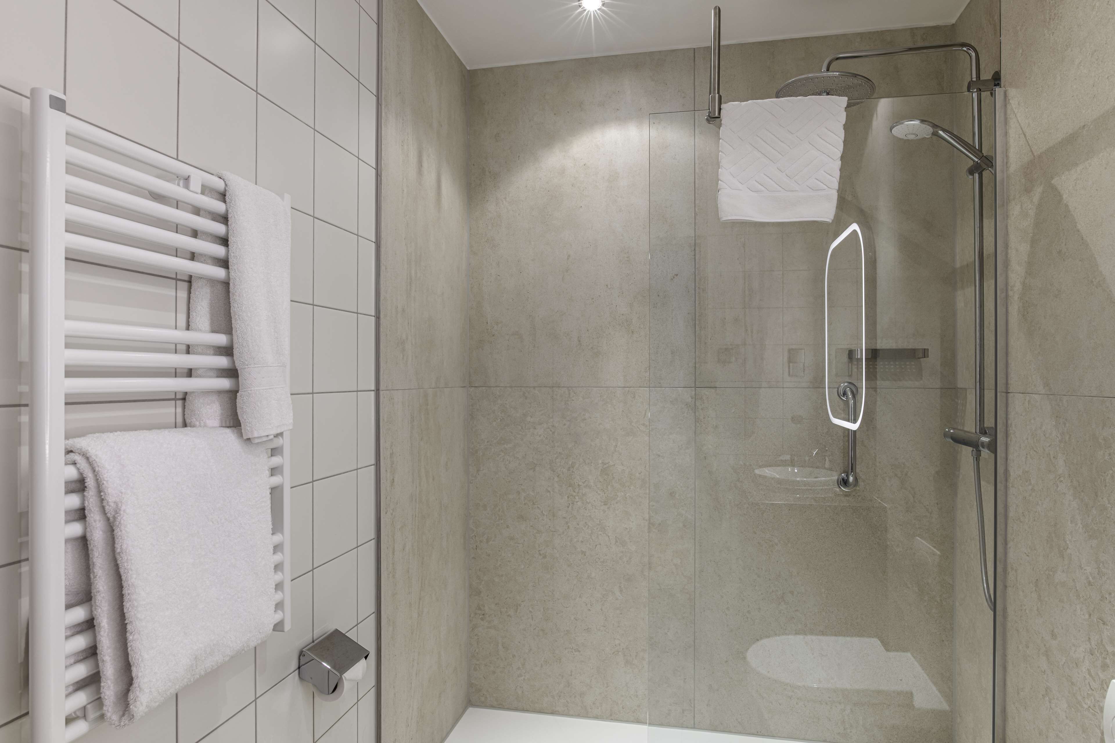 A modern bathroom with a glass-enclosed shower, a white bathtub, and a towel rack with multiple towels.