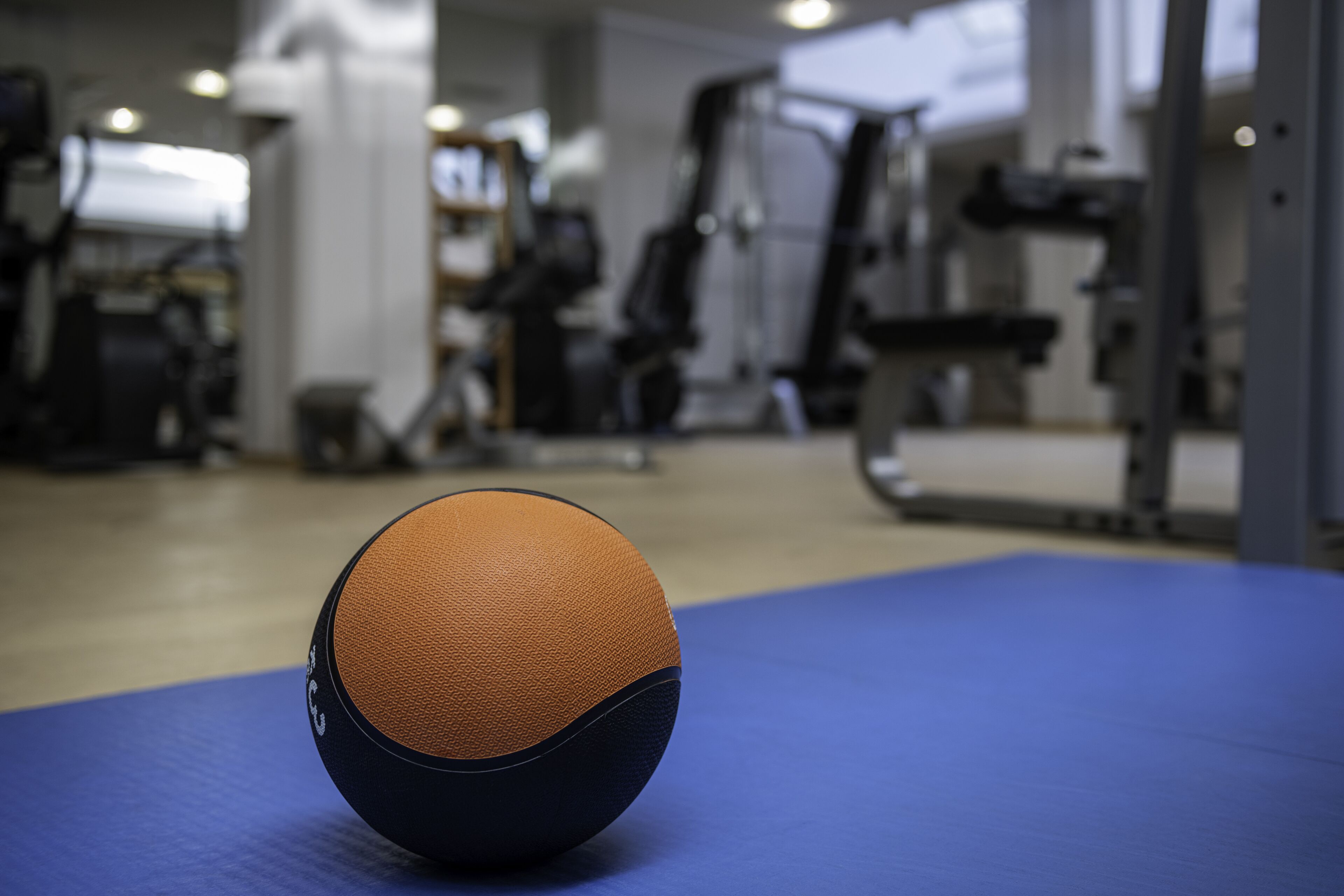 Un ballon de basket sur un tapis bleu, dans une salle de sport où l’on aperçoit en arrière-plan du matériel d’exercice.