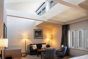 Une chambre d’hôtel moderne, dotée d’un canapé, de fauteuils, d’une table basse, d’un bureau et d’une grande fenêtre avec des rideaux.