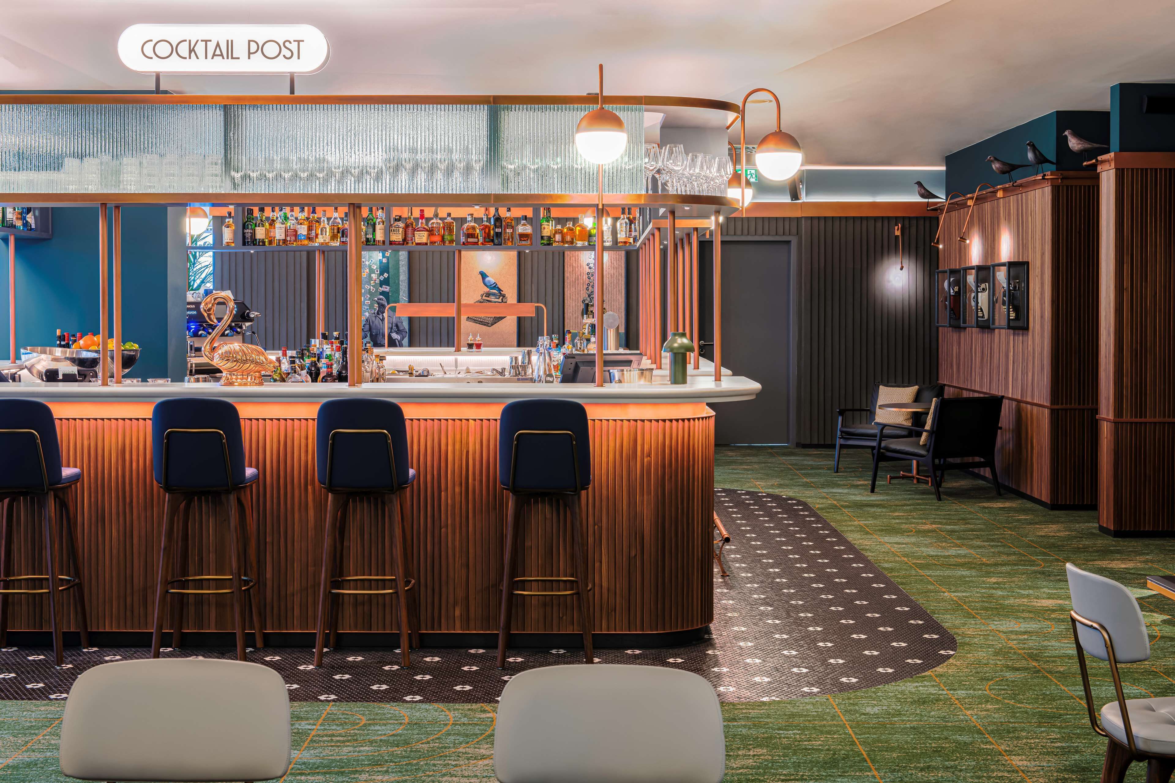 Una zona de bar con mostrador de madera, varios taburetes y una variedad de botellas y vasos.
