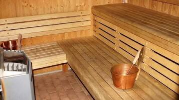 A sauna with wooden benches and a copper bucket.