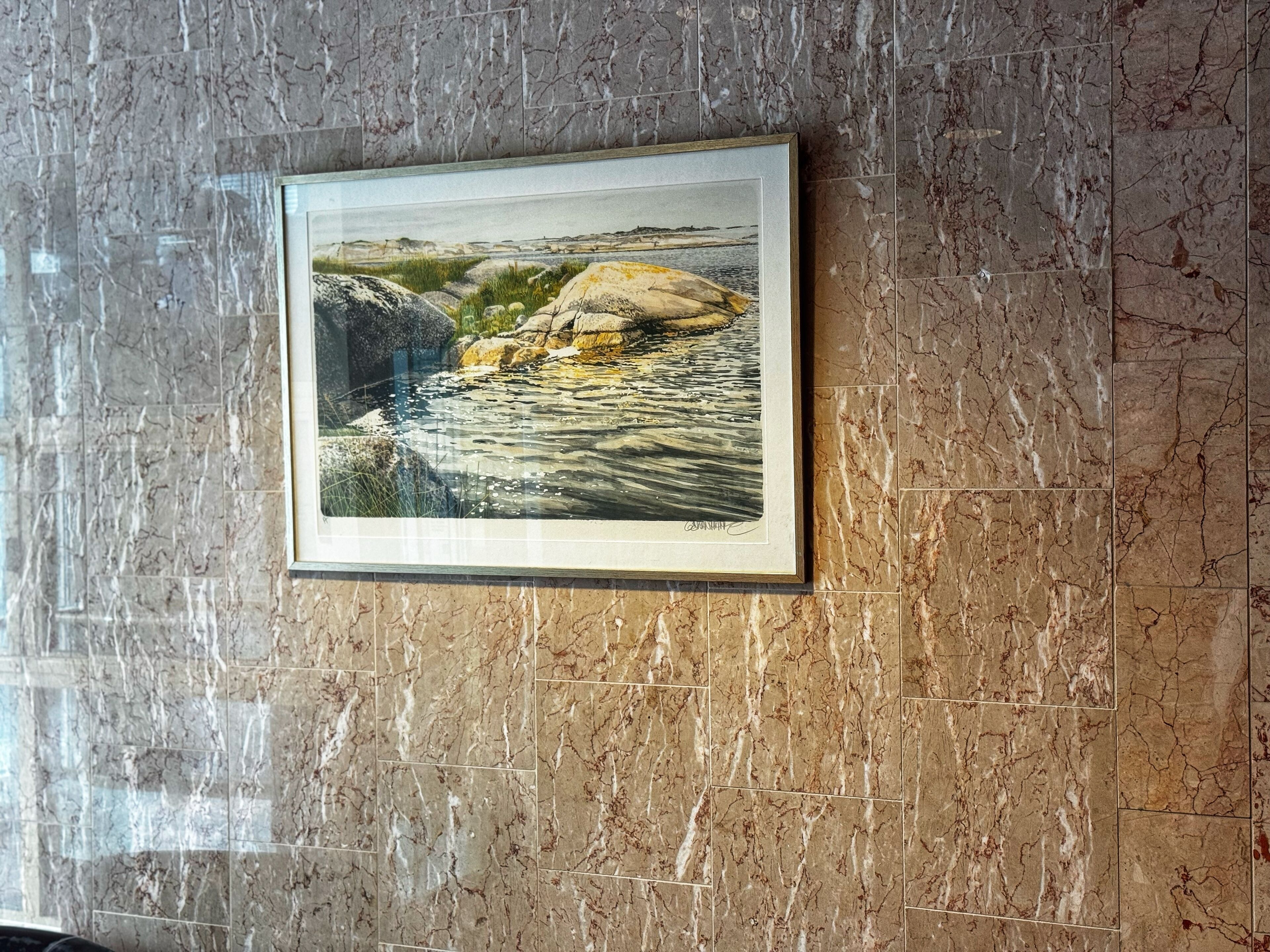 A framed landscape painting on a marble wall.