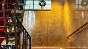 Una escalera de mármol con alfombra roja, barandales de metal y una planta en maceta en la plataforma.