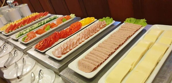 A buffet with various food items including sliced meats, vegetables, and cheese.