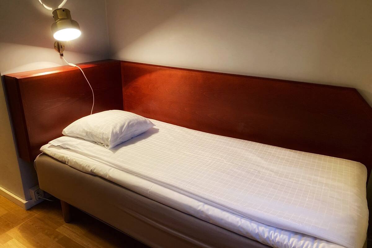 A single bed with a wooden headboard, a white pillow, and a bedside lamp.