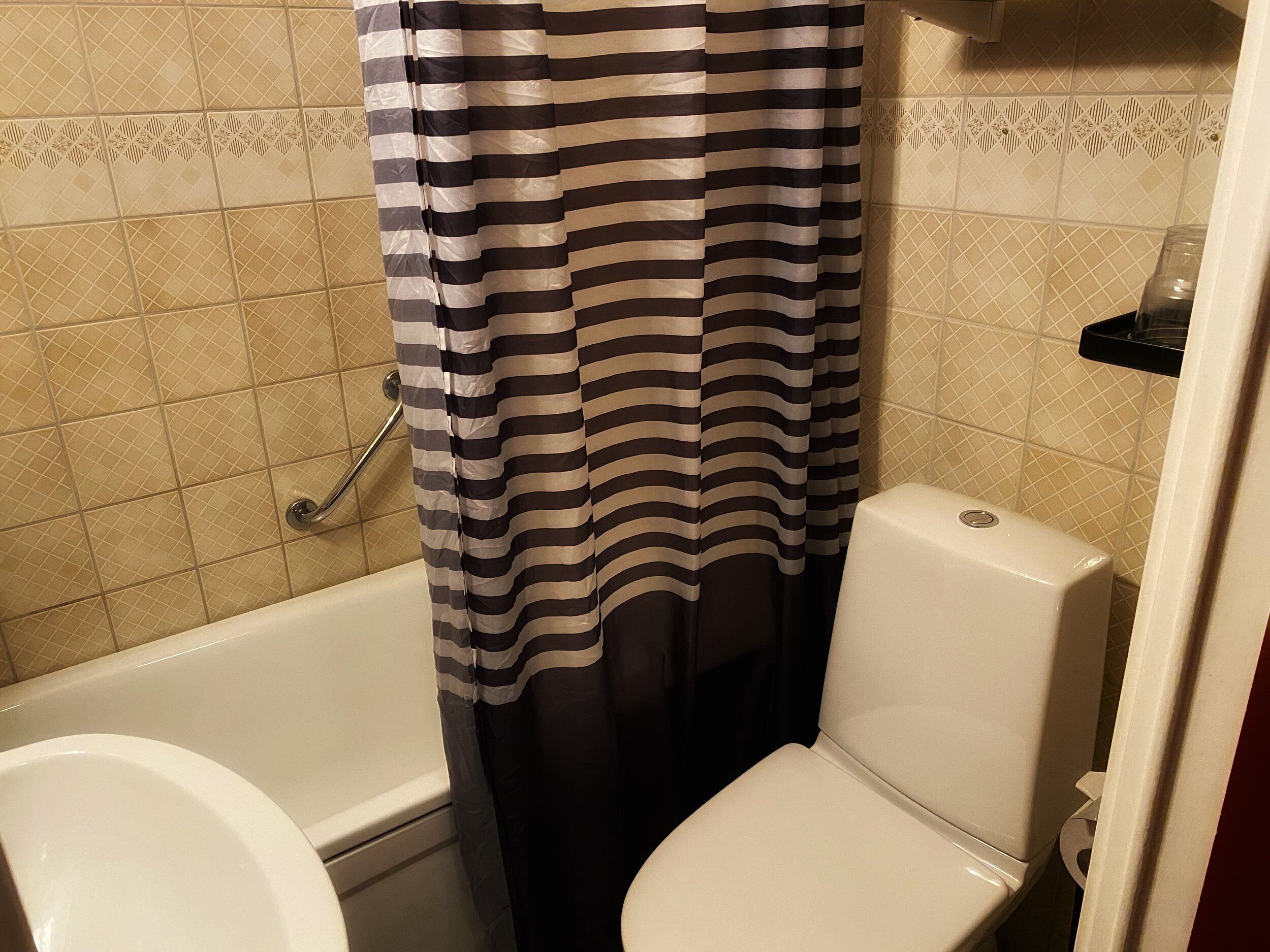 Un baño con una bañera blanca, un inodoro y una cortina de ducha a rayas.