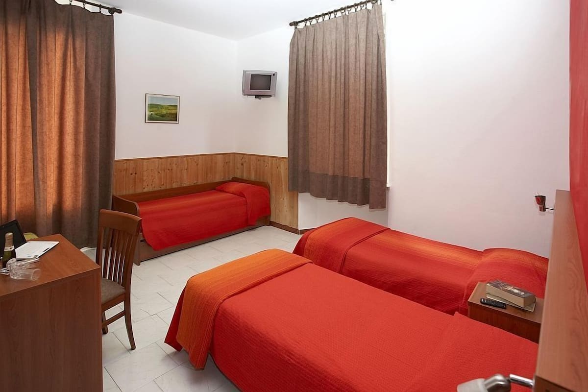 A room with two single beds, a desk with a chair, a television, and a small table with a remote control.