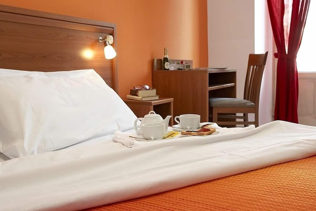 A neatly made bed with white linens, a tray with breakfast items, a bedside table with a book and glasses, and a wooden headboard.