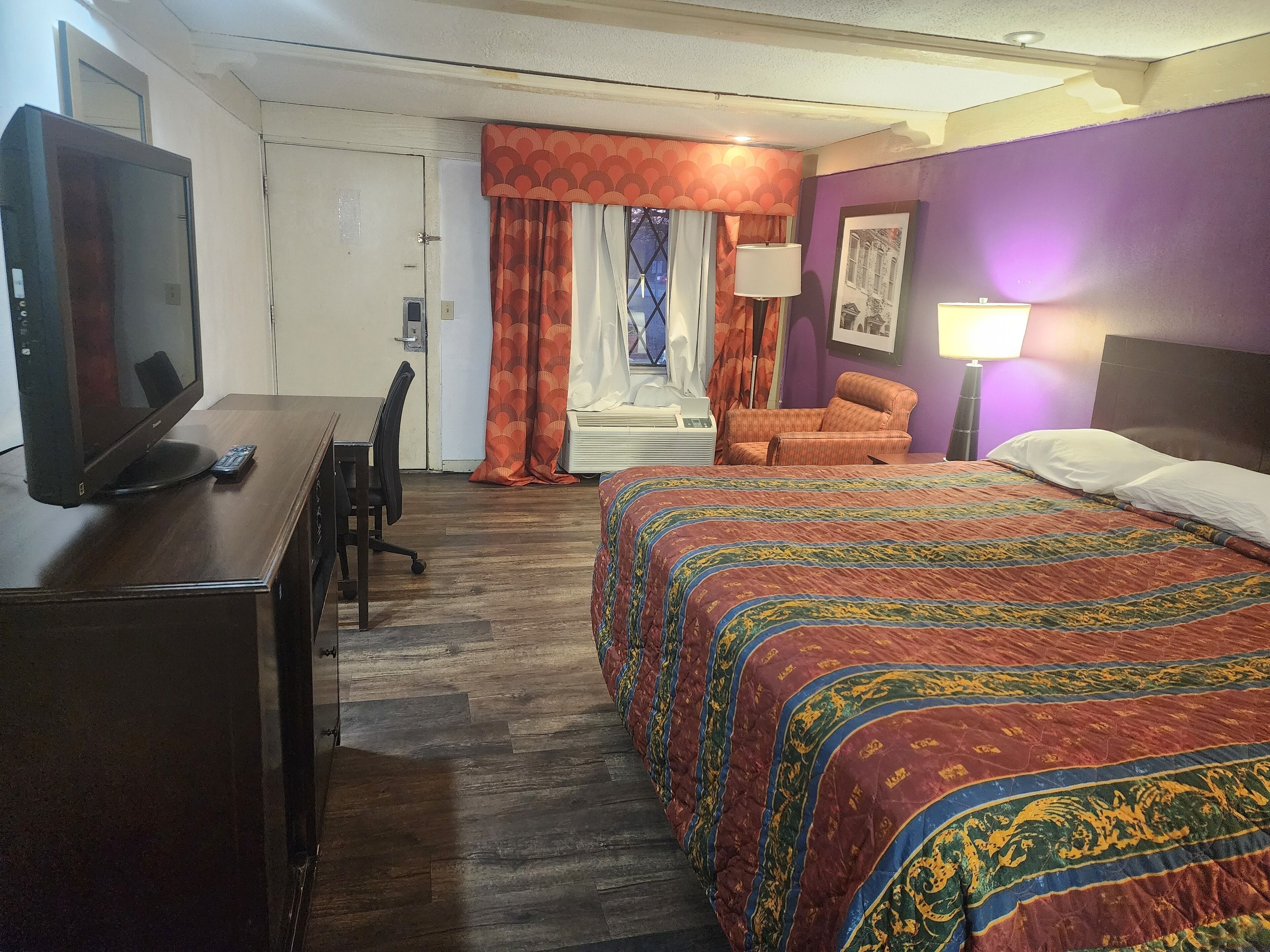 Una camera d'albergo con un letto, una scrivania, una televisione, una poltrona e una finestra con tende.